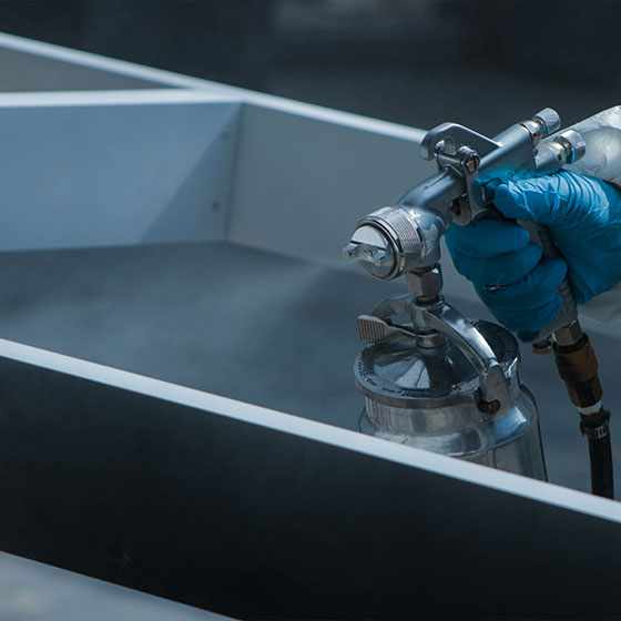 An up-close shot of a professional paint gun in use, spraying forwards onto a plank of wood.